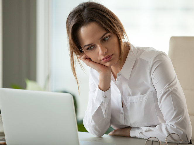 Professional woman resting head in her hand at desk in front of laptop